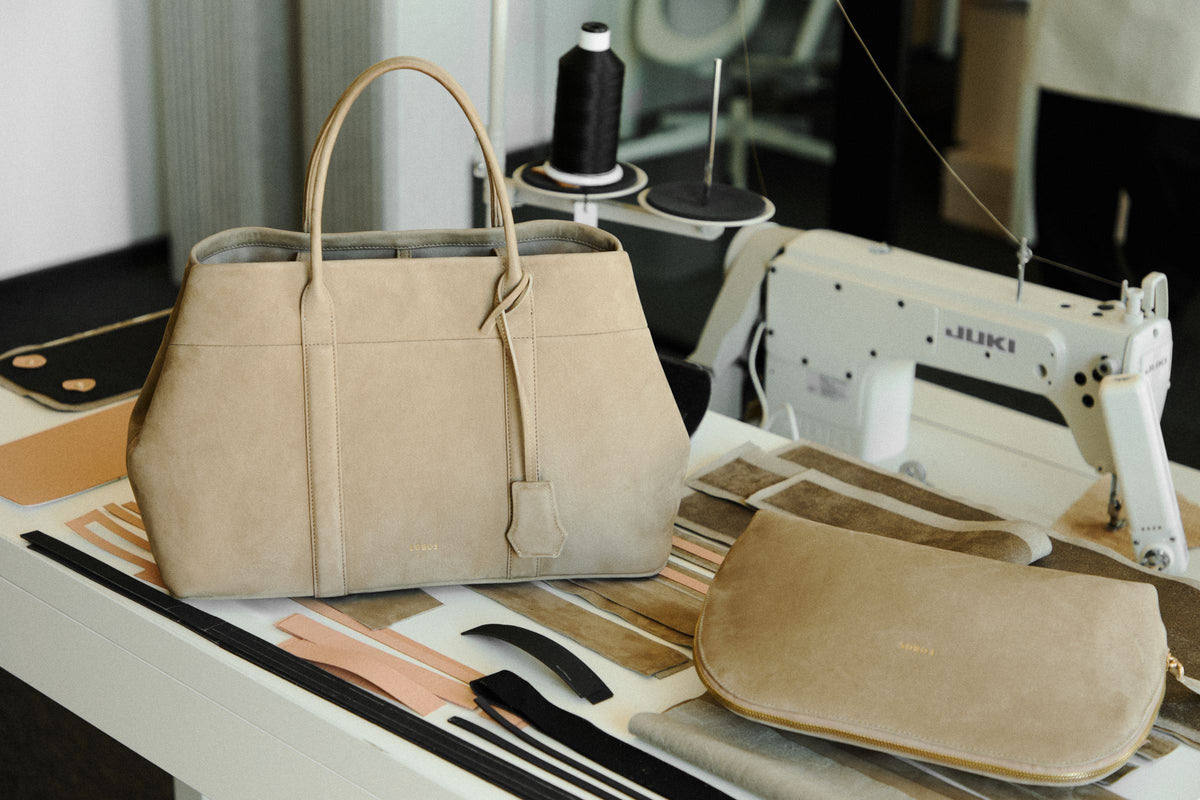 Torebka LE CHIC Iconic na stole w pracowni, obok przycięte elementy ze skóry i maszyna do szycia JUKI